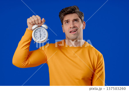 Woken Up By Alarm Clock Sleepy Mature Man Holding It In Hand. Blue Background Woken Up By Alarm Clock Sleepy Mature Man Holding It In Hand. Blue Background 137583260