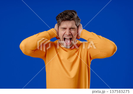 Mature man Covering Ears, Showing Irritation In Blue Studio. Stress, Overload Mature man Covering Ears, Showing Irritation In Blue Studio. Stress, Overload 137583275
