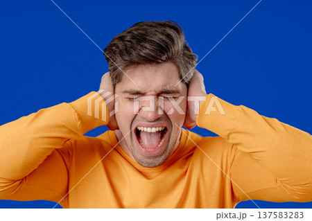 Man in yellow reacts with frustration by blocking out noise or unwanted information. Stress, overload, conflict, workplace disagreement, rejection of opinions in business context. Man in yellow reacts with frustration by blocking out noise or unwanted information. Stress, overload, conflict, workplace disagreement, rejection of opinions in business context. 137583283