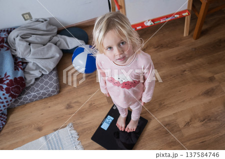 Cute 4 year old Caucasian girl standing on weighing scales  137584746