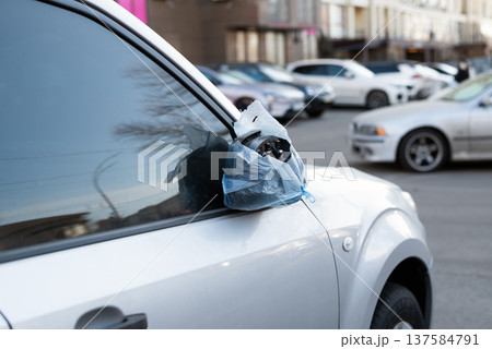 Damaged car side mirror wrapped in a blue plastic bag on a silver vehicle parked in a city street. Damaged car side mirror wrapped in a blue plastic bag on a silver vehicle parked in a city street. 137584791