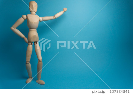 Wooden mannequin stands on blue background with arm raised to the side while posing in a creative way for art or design 137584841