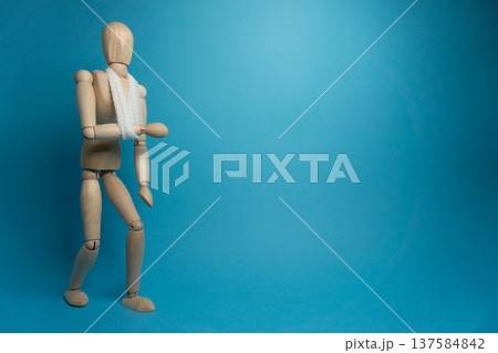 Wooden mannequin holds up an arm in front of blue background while wearing a scarf and facing slightly to the side 137584842