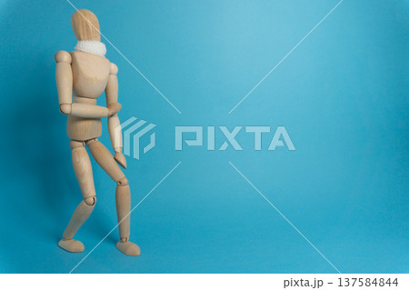 Wooden figure stands against a blue background while holding its arm in a specific pose during a creative art session Wooden figure stands against a blue background while holding its arm in a specific pose during a creative art session 137584844