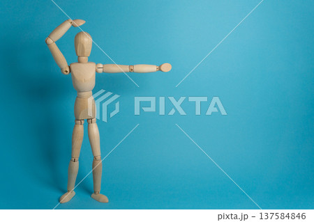 Wooden figure poses with arm raised against a blue background in a studio setting 137584846