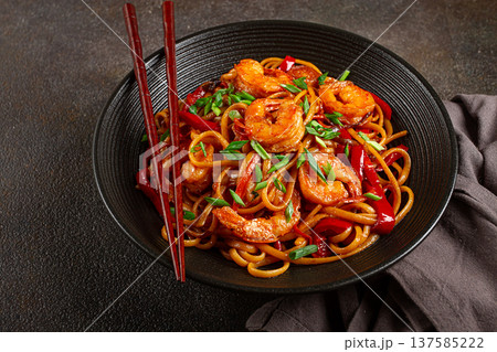 udon stir-fry shrimp noodles with red bell pepper and green onion, served in a black bowl, with chopsticks, dark background, 137585222