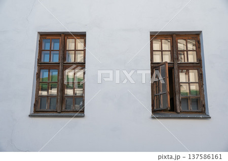 Two wooden windows with glass panes on white building facade, one window open reflecting surrounding architecture in daylight. Architecture detail, real estate exterior, renovation concept Two wooden windows with glass panes on white building facade, one window open reflecting surrounding architecture in daylight. Architecture detail, real estate exterior, renovation concept 137586161