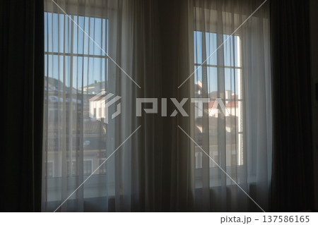 Hotel room window with sheer curtains and city view through glass in modern accommodation interior. Travel stay, hospitality design, urban hotel comfort, tourism lodging 137586165
