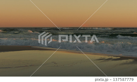 Sunset illuminating ocean waves, creating a serene atmosphere with reflections on wet sand and gentle surf sounds 137587779