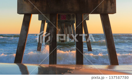 Pier structure stands tall over ocean waves at sunset, creating a serene atmosphere with reflections on wet sand and vibrant colors in the sky Pier structure stands tall over ocean waves at sunset, creating a serene atmosphere with reflections on wet sand and vibrant colors in the sky 137587780