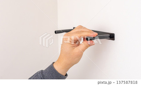 Mans hand using black marker to mark line on white wall above black shelf bracket. Home improvement, measuring and marking, DIY level indication, precise preparation. 137587818