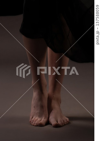 Woman in dark dress stands barefoot on plain surface, showing only legs and feet 137588059