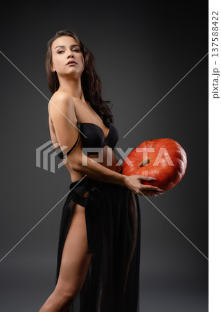 Beautiful woman poses with a pumpkin under dramatic lighting Beautiful woman poses with a pumpkin under dramatic lighting 137588422