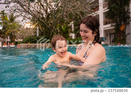 Caucasian woman holds her son while swimming in a pool on vacation. Mom teaches little boy to swim. Caucasian woman holds her son while swimming in a pool on vacation. Mom teaches little boy to swim. 137588630