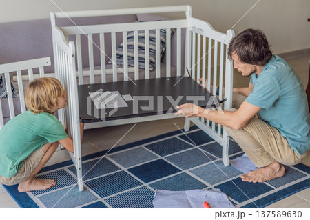 Father and older brother assembling a baby crib at home, preparing for a newborn arrival. Warm family moment full of care and anticipation. Parenthood, sibling bond and home preparation concept 137589630