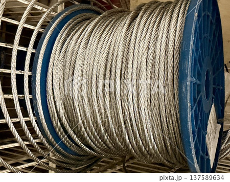 Steel wire rope wound on blue spool in hardware store or industrial setting. Steel wire rope wound on blue spool in hardware store or industrial setting. 137589634