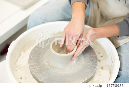 Close-up of woman's hands shaping clay on pottery wheel Close-up of woman's hands shaping clay on pottery wheel 137589884