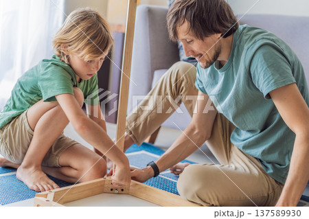 Father and his son assembling a table together in the living room at home. Meaningful family moment showing teamwork, learning and support. Fatherhood, home improvement and bonding through shared Father and his son assembling a table together in the living room at home. Meaningful family moment showing teamwork, learning and support. Fatherhood, home improvement and bonding through shared 137589930
