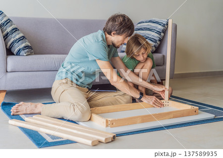Father and his son assembling a table together in the living room at home. Meaningful family moment showing teamwork, learning and support. Fatherhood, home improvement and bonding through shared Father and his son assembling a table together in the living room at home. Meaningful family moment showing teamwork, learning and support. Fatherhood, home improvement and bonding through shared 137589935