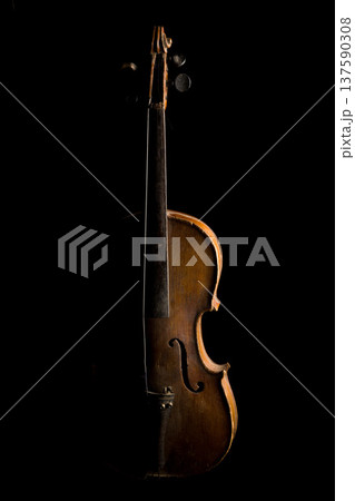 Antique violin displayed against a dark background highlighting its curves and craftsmanship in warm lighting 137590308