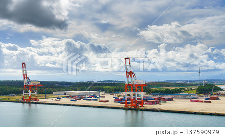 Sakata, Yamagata, Japan - Oct 5 2024, panoramic aerial view from sea of  docks with cranes and containers of port of Sakata, with a forest in background and cloudy sky above, at daytime, Sakata, Japan 137590979