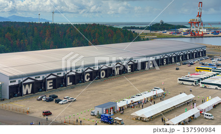 Sakata, Yamagata, Japan - Oct 5 2024, panoramic aerial view of hangars of port of Sakata, on facade of which is written Welcome to Sakata, a market nearby and tourist buses are parked, Sakata, Japan 137590984