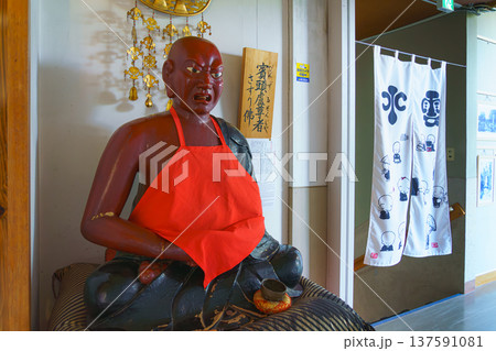 Sakata, Yamagata, japan - Oct 5 2024, Close-up view of a wooden Pindola Bharadvaja statue in a lotus position with an aggressive face wearing a red bib, at Jichi-in Temple, Sakata, Japan 137591081