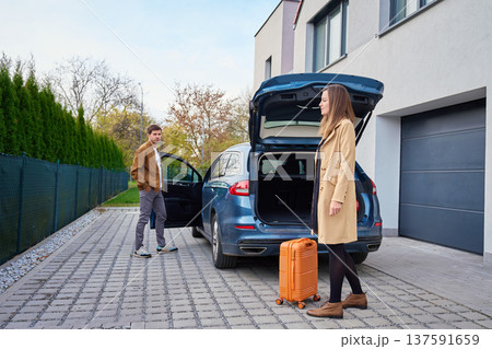 Man and woman standing near car with open trunk and suitcase outside building 137591659