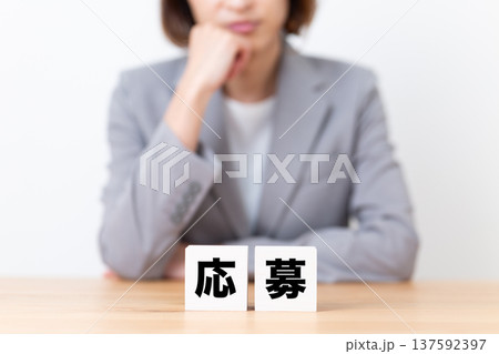 応募のブロックと悩むスーツ姿のミドル女性 応募のブロックと悩むスーツ姿のミドル女性 137592397