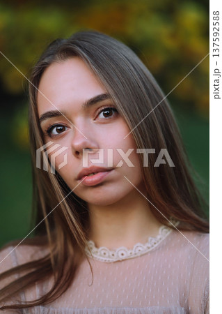 Close up portrait of a beautiful young woman with long hair and brown eyes in autumn park 137592588