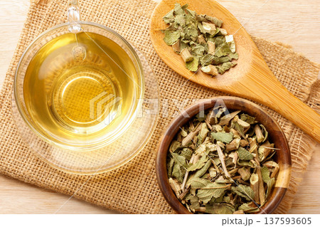 A glass cup of lemon balm tea, surrounded by dried leaves in a bowl, and a wooden spoon placed on burlap fabric A glass cup of lemon balm tea, surrounded by dried leaves in a bowl, and a wooden spoon placed on burlap fabric 137593605