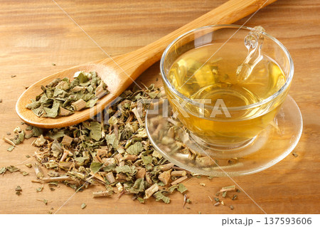 A glass cup of lemon balm tea, surrounded by dried leaves in a bowl, and a wooden spoon 137593606