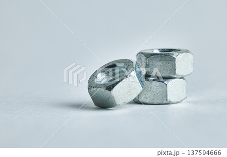 Macro view of three galvanized metal nuts stacked on a neutral white background with shadows Macro view of three galvanized metal nuts stacked on a neutral white background with shadows 137594666
