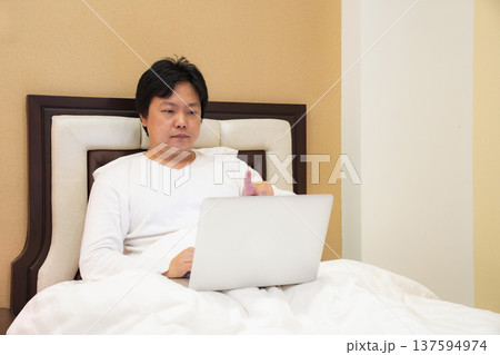 A man enjoys his time online while resting in bed. The image conveys comfort, freedom, and how technology blends with everyday life. A man enjoys his time online while resting in bed. The image conveys comfort, freedom, and how technology blends with everyday life. 137594974