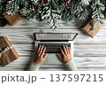 Laptop mockup with blank screen and hands typing, surrounded by holiday decor, pine branches, and festive gifts 137597215