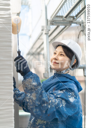外壁塗装の現場で働く女性職人：笑顔でローラー塗装を行う施工風景 137599050