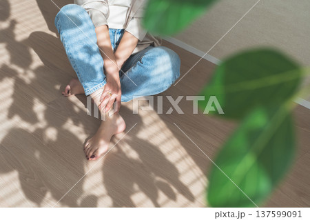 西陽の当たるフローリングの床に座るデニム姿の女性 137599091