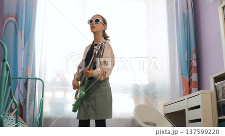Girl enjoys playing electric guitar at home wearing sunglasses, immersing herself in music and creative expression Girl enjoys playing electric guitar at home wearing sunglasses, immersing herself in music and creative expression 137599220