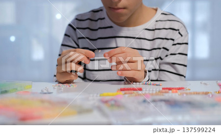 A teenage girl works on a beaded bracelet at her desk threading beads and organizing colorful supplies with care and creativity A teenage girl works on a beaded bracelet at her desk threading beads and organizing colorful supplies with care and creativity 137599224