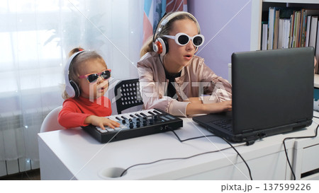 Two girls enjoy making music at home together. Older sister plays midi keyboard while younger follows along, focused on their craft 137599226