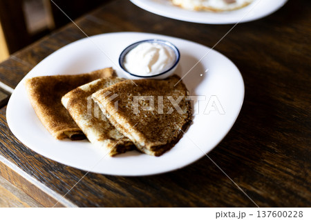 Delicious homemade pancakes served on a plate with sour cream on a dark background creating a cozy rustic food atmosphere 137600228
