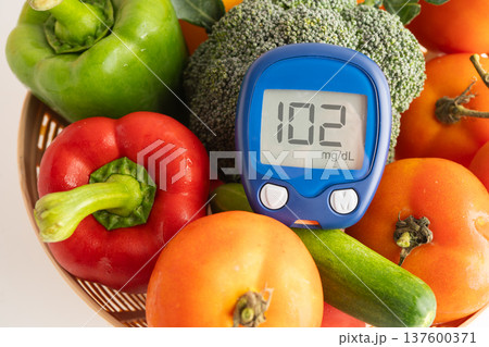 Asian hand holding digital glucose monitor measure with vegetable and fruit healthy food. 137600371
