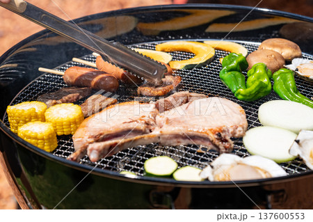 バーベキューを楽しむ トングで焼き加減を見る バーベキューを楽しむ トングで焼き加減を見る 137600553