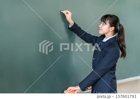 教室の黒板にチョークで文字を書く中学生の女子生徒 137601791