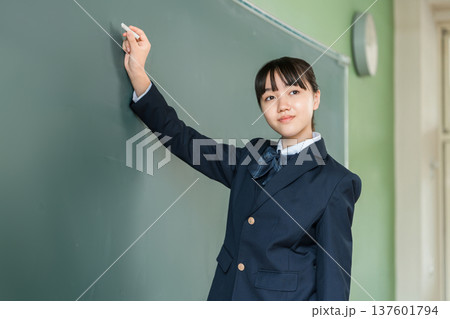 教室の黒板にチョークで文字を書く中学生の女子生徒 137601794