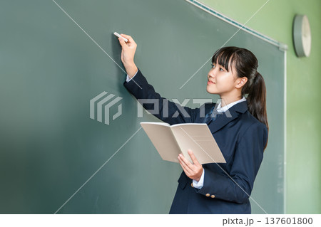 教室の黒板にチョークで文字を書く中学生の女子生徒 教室の黒板にチョークで文字を書く中学生の女子生徒 137601800