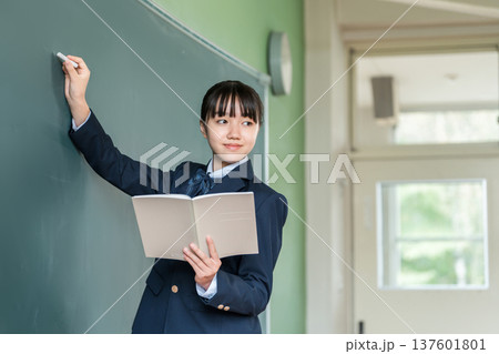 教室の黒板にチョークで文字を書く中学生の女子生徒 教室の黒板にチョークで文字を書く中学生の女子生徒 137601801