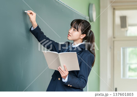教室の黒板にチョークで文字を書く中学生の女子生徒 教室の黒板にチョークで文字を書く中学生の女子生徒 137601803