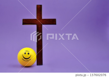 Happy Face Yellow Ball Next To Wooden Cross on Purple Background Copy Space Right Side 137602076