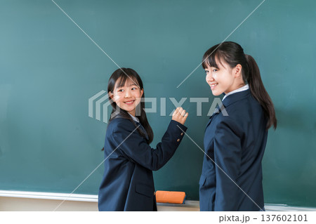 教室の黒板にチョークで文字を書く中学生の女子生徒 教室の黒板にチョークで文字を書く中学生の女子生徒 137602101